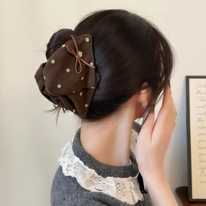 Pince à cheveux nœud marron à pois blancs avec breloque cœur dorée sur un chignon bas