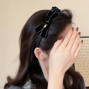 Elegant black velvet bow headband with white stitching and gold detail on a female model