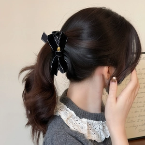 Elegant black velvet bow hair clip with white stitching and gold buckle on a model