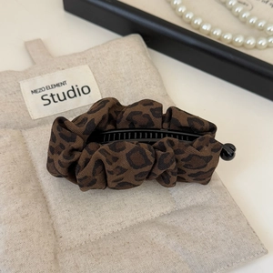 Detail of leopard print fabric banana hair clip with rich texture on a soft linen background