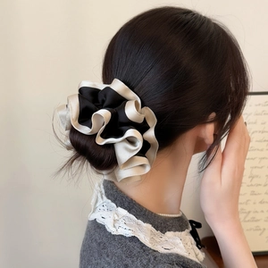 Rear view of a model wearing a dual-tone black and beige satin scrunchie on a low bun