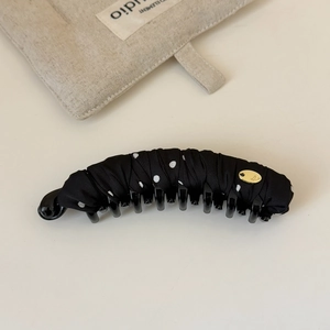 Detail view of a black banana clip with white polka dots and golden metal plate accent