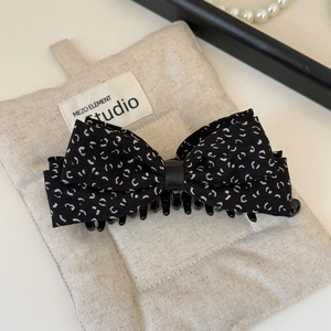 Detail of elegant black fabric bow hair clip with white pattern and secure plastic grip