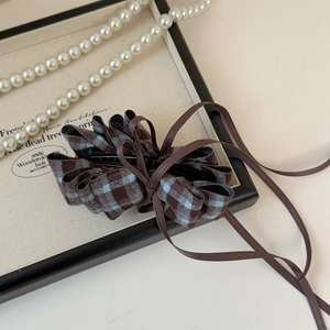 Detail view of a vintage plaid bow banana clip with brown ribbon on a wooden box