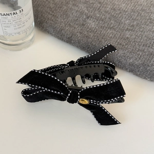 Detail of a black velvet bow hair clip with white stitching and a golden metal emblem