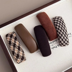 Detailed close-up of retro plaid and leather hair clips on a minimalist wooden tray