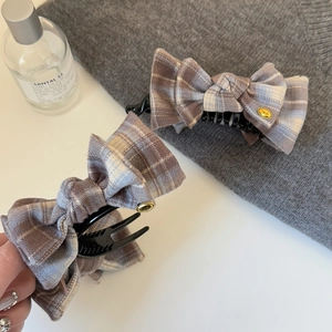 Detail of checkered bow hair clips in brown and blue with elegant gold emblem accents