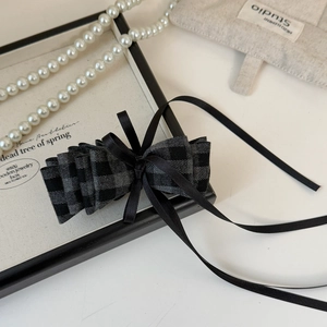 Detail view of a plaid bow banana clip with elegant black ribbons on a wooden display box