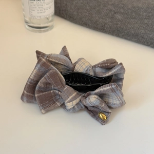 Close-up of brown plaid bow hair claw clip with golden logo on fabric texture