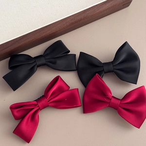 Detail of four satin bow hair clips in black and deep red on a beige background