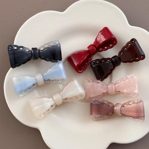 Detail of elegant hollow bow hair clips in multiple colors on a ceramic petal tray