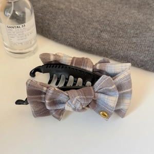 Detail view of a plaid fabric bow banana hair clip with a gold logo tag on a white surface