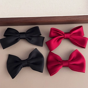 Close-up of black and burgundy satin bow hair clips on a textured beige surface