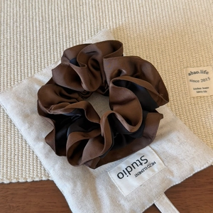 Detail view of dual-color satin scrunchie with ruffled edges on rustic linen background