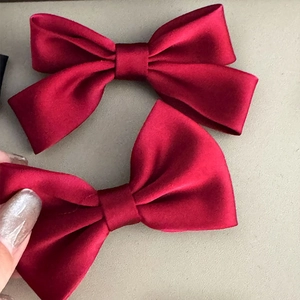 Detail view of two wine red satin bow hair clips with soft matte texture and dual layers