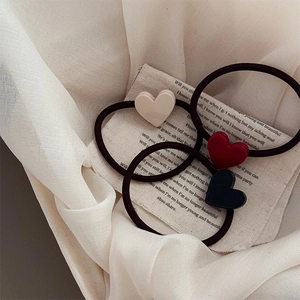 Trois élastiques à cheveux coeur en beige, rouge et noir sur fond de tissu minimaliste