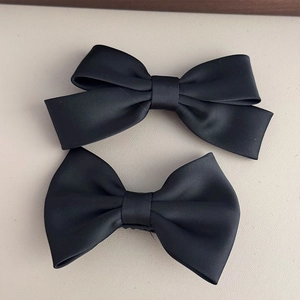 Detail view of two elegant black satin hair clips with double-layered bow design