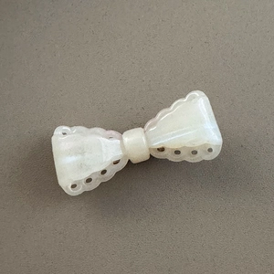 Detailed close-up of a pearly cream bow hair clip with scalloped hollowed edges