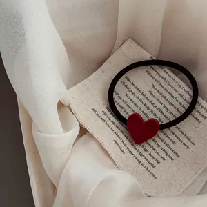 Gros plan du pendentif cœur rouge sur chouchou noir élastique sur fond de tissu vintage