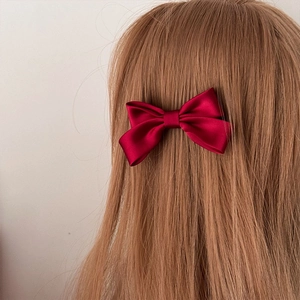 Detail of red satin bow hair clip worn on long brown hair for a festive look