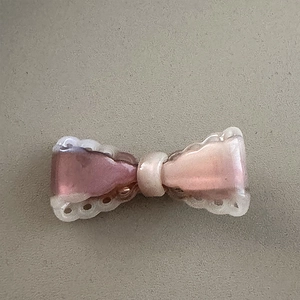Close-up of a pink gradient bow hair clip with white scalloped lace edges and resin finish