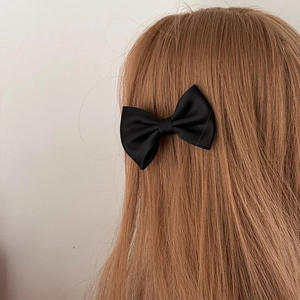 Detail view of a black satin ribbon bow hair clip styled on straight dark hair