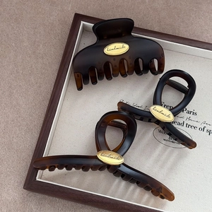 Three tortoise shell hair claws with gold handmade labels on a vintage wooden tray