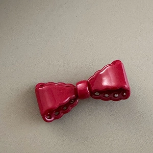 Close-up of a glossy red bow hair clip with decorative hollowed-out scalloped edges