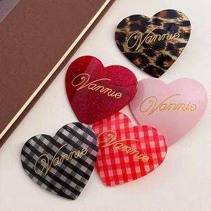Five assorted heart-shaped acetate hair clips with Vannie gold lettering on beige surface