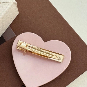 Detail view of the golden metal hair clip back with non-slip teeth on a pink tray