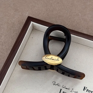 Detailed macro view of tortoiseshell hair claw clip with golden handmade logo plate