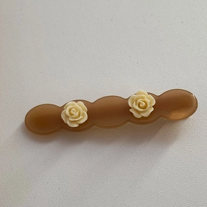 Detailed view of acetic acid rose hair clip with caramel wavy base and cream flowers