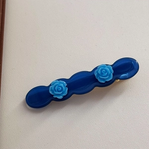 Detailed view of dark blue acetate hair clip featuring light blue 3D rose flower accents