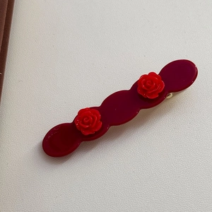 Detailed macro view of acetate wavy hair clip with 3D red roses and metallic fastener