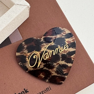 Macro detail of heart-shaped acetate hair clip featuring brown leopard print and gold logo