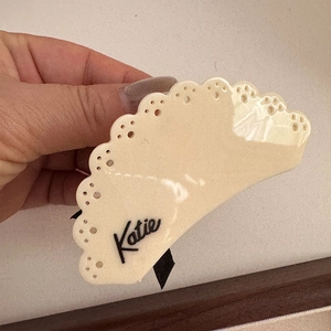 Dettaglio della molletta per capelli in acetato crema con design traforato e logo Katie