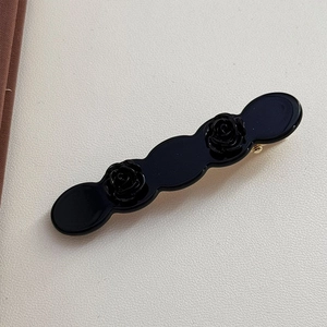 Close-up of black acetate rose flower hair clips on a textured cream surface