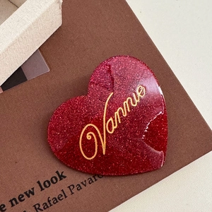 Close-up of heart-shaped red glitter acetate hair clip with golden Vannie lettering