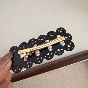 Dettaglio del nastro rosa intrecciato nel fermaglio in pizzo nero con clip in metallo oro
