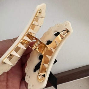 Dettaglio del fermaglio per capelli in acetato crema con fiocco nero e molla dorata