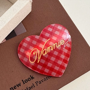Macro detail of red plaid heart-shaped acetate hair clip with Vannie lettering