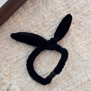 Détail d'un chouchou en velours noir à oreilles de lapin sur fond textile texturé