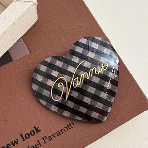 Close-up of heart-shaped acetate hair clip featuring black grey plaid and gold Vannie text