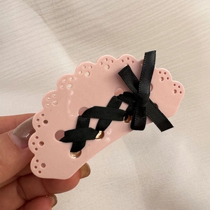 Dettaglio della molletta rosa con fiocco di nastro nero e trama traforata tipo pizzo