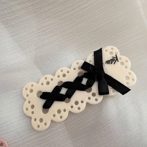 Dettaglio del fermaglio per capelli crema con nastro nero intrecciato e logo Katie