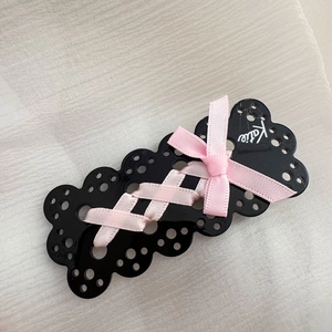 Dettaglio della molletta nera traforata con nastro rosa intrecciato e scritta Katie