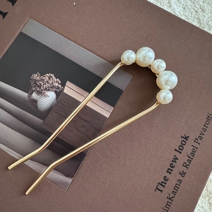 Detailed close-up of golden U-shaped hair pin with pearls on vintage magazine