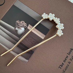 Detail of elegant gold U-shaped hair pin with white pearl flower decor on a magazine