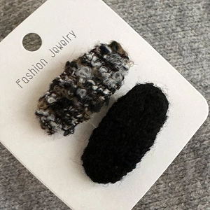 Detail von gestrickten ovalen Haarklammern in Schwarz und Tweed auf Displaykarte