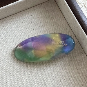 Close-up of handmade oval acetate hair clip featuring colorful gradient and gold logo